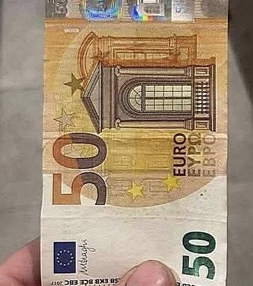 Купюра в 50 євро між пальців на сірому фоні — символ готівкової валюти