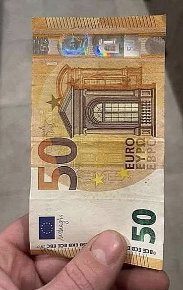 Купюра в 50 євро між пальців на сірому фоні — символ готівкової валюти