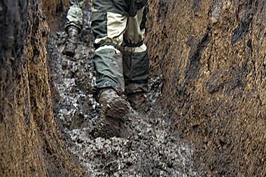 ноги бійця у брудному окопі під час війни, небезпечні умови на передовій