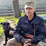 Сергій Русінов сидить на лавці з автоматом у руках, поруч стоїть собака