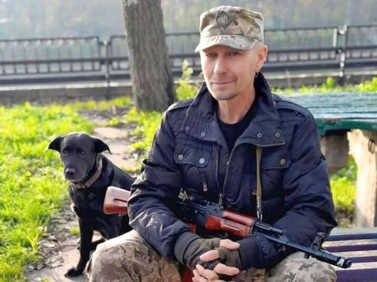 Сергій Русінов сидить на лавці з автоматом у руках, поруч стоїть собака